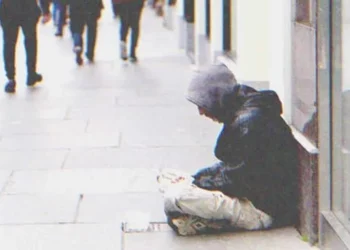 Egy könnyes szemű fiatal nő egy bankjegyet dob a koldusnak, aki kibontja és egy feliratot lát: „Segíts nekem!”